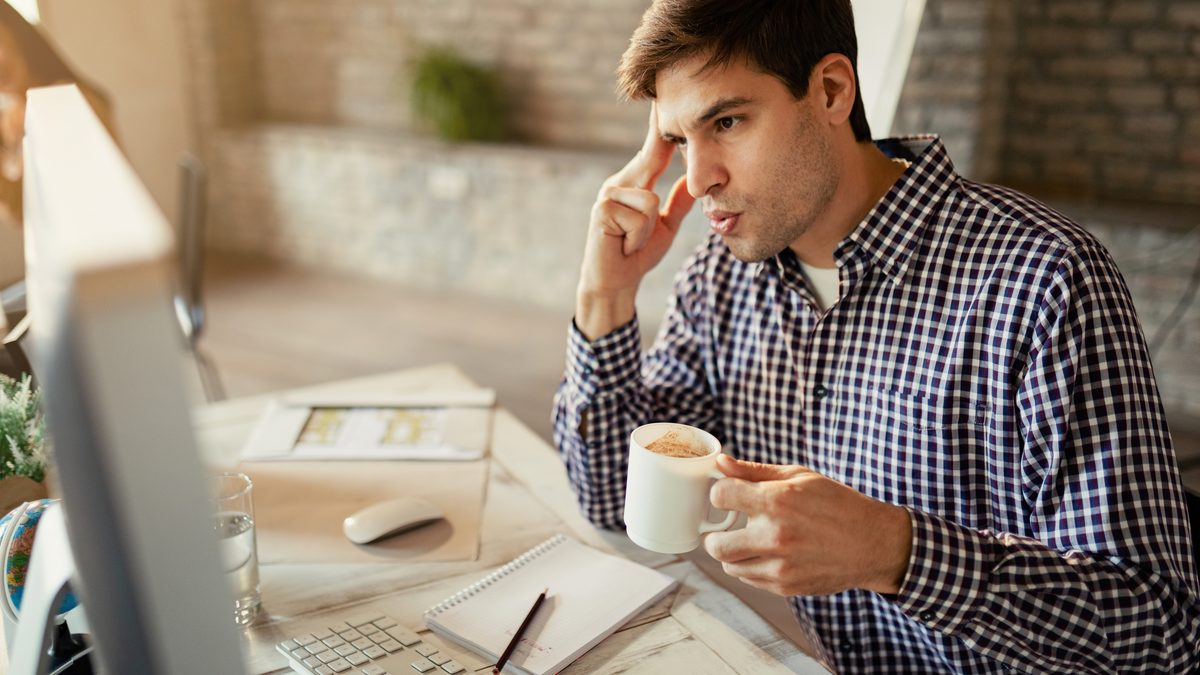 Comerciante conferindo um comprovante de transferência no celular ao lado do computador do caixa